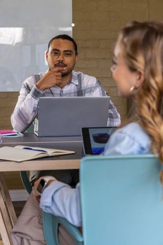 Coworkers discussing project around meeting table with laptop, tablet, notebooks