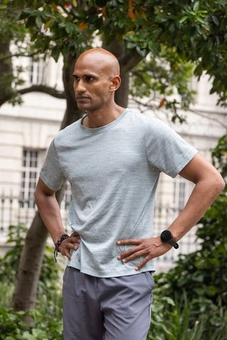 African american man standing beneath leafy canopy in urban courtyard wearing wristwatch