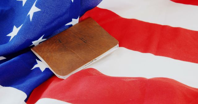 An old book rests on the American flag, symbolizing the rich history and foundational values of the United States, with copy space. The image evokes a sense of patriotism and respect for the country's heritage.