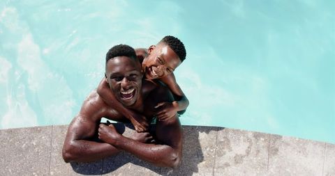 Father and son enjoying fun swimming in bright pool together