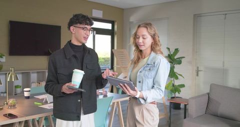 Young diverse coworkers reviewing tablet holding coffee cup in bright modern coworking office