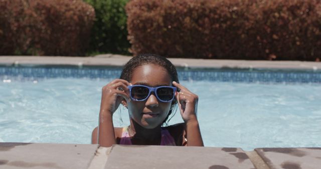 Happy biracial girl in sunglasses relaxing in swimming pool in the sun. Summer, vacations, childhood, fun and free time, unaltered.
