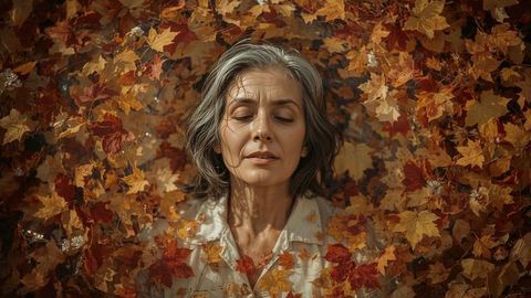 Senior woman relaxing in autumn leaves – peaceful elderly lady lying in fall nature park