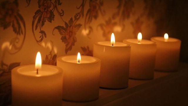Five glowing pillar candles casting warm ambient light on mantel with vintage floral wallpaper