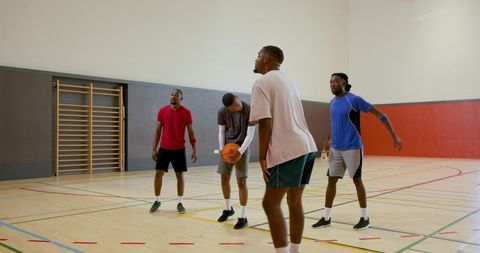Young men practicing basketball drill on indoor gym court, teamwork and defense training