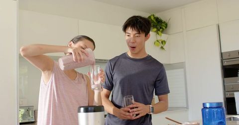 Couple pouring berry smoothie at modern kitchen island, woman pouring, man reacting
