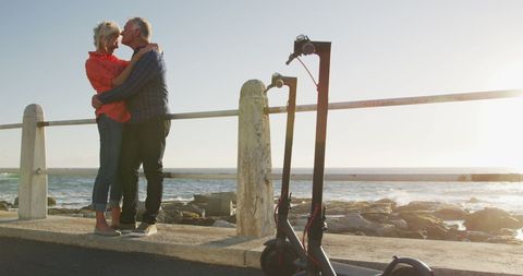 Senior Couple Embracing on Sunny Seafront Promenade with Scooters