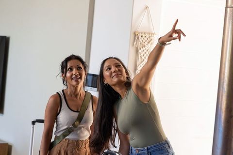 Diverse women pointing and arriving in modern apartment with luggage and minimal decor