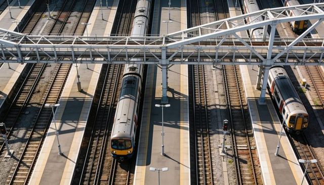 Sunlit commuter trains waiting on urban rail terminal with overhead pedestrian bridge