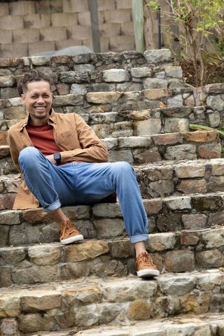 Smiling man sitting on stone steps wearing smartwatch, denim jeans and sneakers