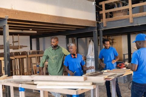 African american carpentry team measuring and building woodwork in industrial workshop