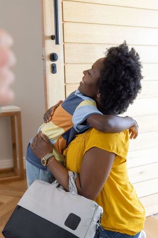 African american mother and son reuniting with warm hug at home entryway, carrying bag