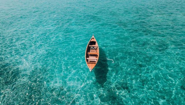 Aerial wooden rowboat floating on turquoise sea with mooring rope and shadow