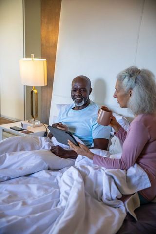 Senior Couple Relaxing with Tablet and Coffee in Bed