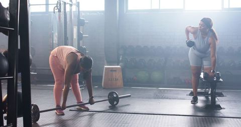 Diverse women training with barbell and dumbbell in industrial gym, partners focused