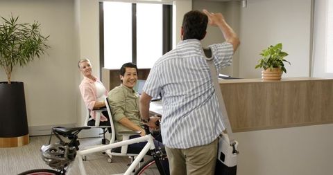 Professional entering office with bicycle greeting team