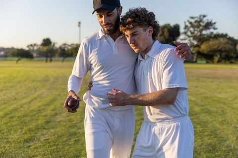 Cricket teammates supporting each other while walking across sunlit field after match