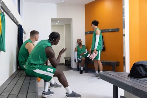 Basketball team talking and resting in locker room wearing green uniforms after game