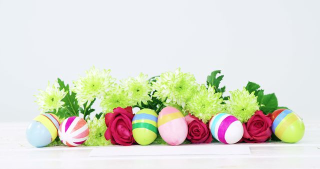 Colorful Easter eggs and vibrant flowers are arranged on a surface, with copy space. This festive setup symbolizes the celebration of Easter and the arrival of spring.