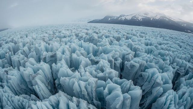 Serrated glacier field stretching toward distant snowy peaks with towering blue ice spires
