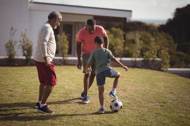 Three generations of a family enjoying a game of soccer in the garden. The boy is actively engaged with his father and grandfather, promoting family bonding and physical activity. Ideal for use in advertisements, family-oriented content, health and wellness promotions, and lifestyle blogs.