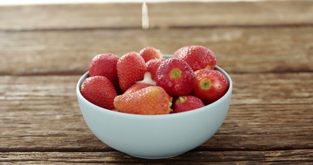 Fresh strawberries in a white bowl placed on a wooden table. This image can be used for healthy eating, organic food promotion, summer recipes, or rustic kitchen decor themes.