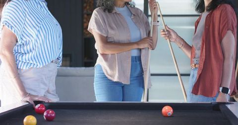 Three women playing pool in contemporary game room, casual friends socializing