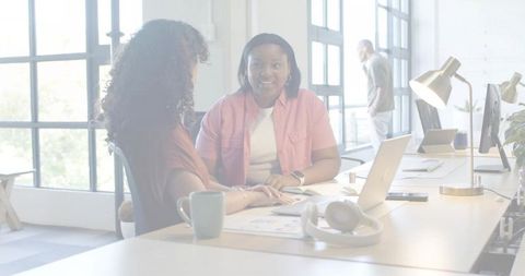 Women collaborating over charts and laptop in bright modern coworking office space