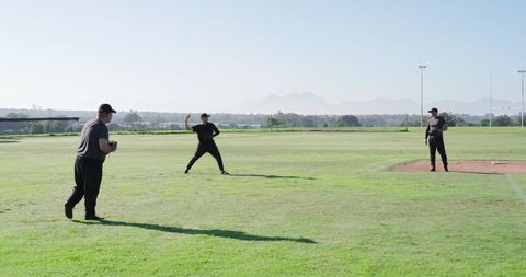 Baseball teammates practicing pitching and fielding on sunny outfield with open sky