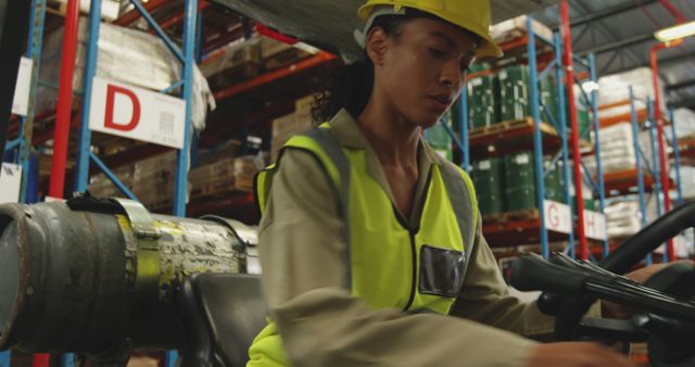 Female warehouse worker wearing yellow vest and hard hat operating forklift in industrial storage. Ideal for depicting female employment in logistics, warehouse operations, retail logistics, safety procedures, and industrial workforce.