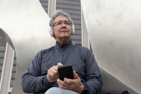 Senior asian man listening to music with headphones while using smartphone in urban plaza