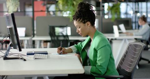 African American Businesswoman Writing at Desk in Modern Open-Plan Coworking Office