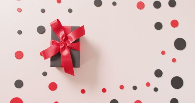 High angle view of black gift box with red ribbon on white with red and black dots and copy space. Luxury treat, present, shopping, black friday sale and retail concept digitally generated image.