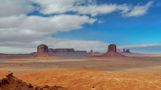 Majestic view of Monument Valley showcasing towering sandstone buttes under a partly cloudy sky. Ideal for use in travel guides, tourism advertisements, and nature blogs. Highlights the natural beauty and iconic features of the American Southwest, capturing the vastness and serene atmosphere of the desert.
