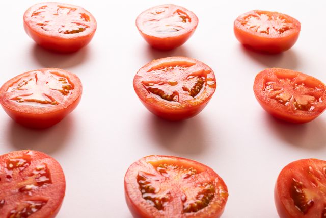 High angle view of fresh tomato halves arranged on a white background. Ideal for use in food blogs, healthy eating articles, organic produce promotions, and culinary websites. Perfect for illustrating concepts related to nutrition, diet, and natural ingredients.