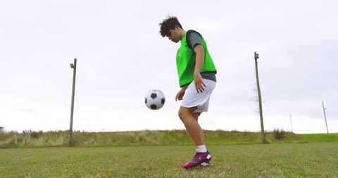 Teenage Boy Juggling Soccer Ball on Outdoor Field in Green Vest