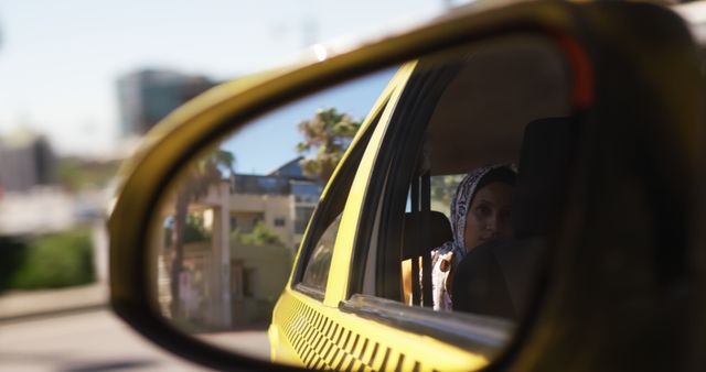 Reflection of woman in a taxi's side mirror; provides urban and travel themes. Useful for illustrating concepts such as transportation, contemplation, city life, or travel experiences. Ideal for websites, blogs, or promotional materials related to travel services, urban exploration, or automobile industries.