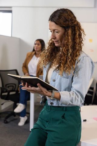 Curly-haired woman reading notebook while leading collaborative office discussion