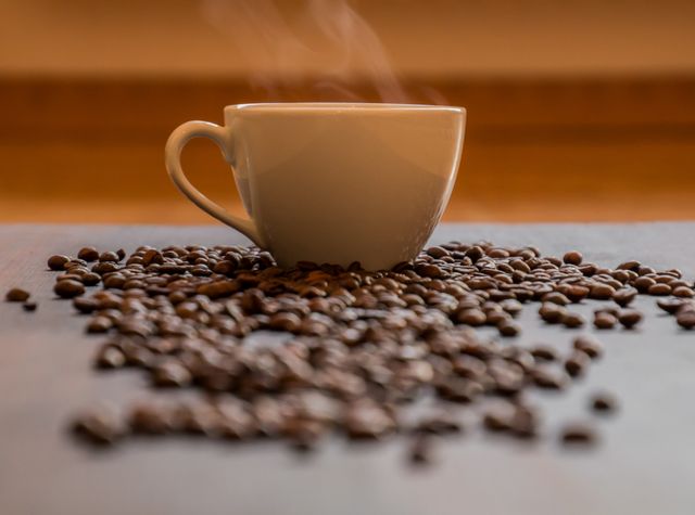 Steaming Cup of Coffee with Scattered Beans in Warm Light - Download Free Stock Photos Pikwizard.com