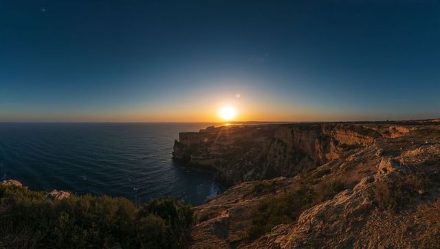 Sun setting over rugged coastal cliffs with panoramic ocean vista at dusk