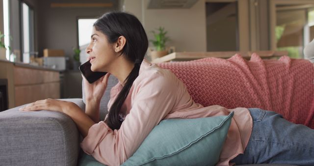 Image of happy biracial woman lying on sofa and having call. Relax, leisure and spending free time at home with technology concept.