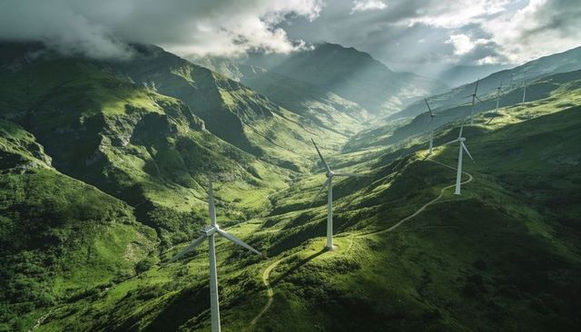 Wind turbines on misty mountain ridge generating renewable energy over winding access road