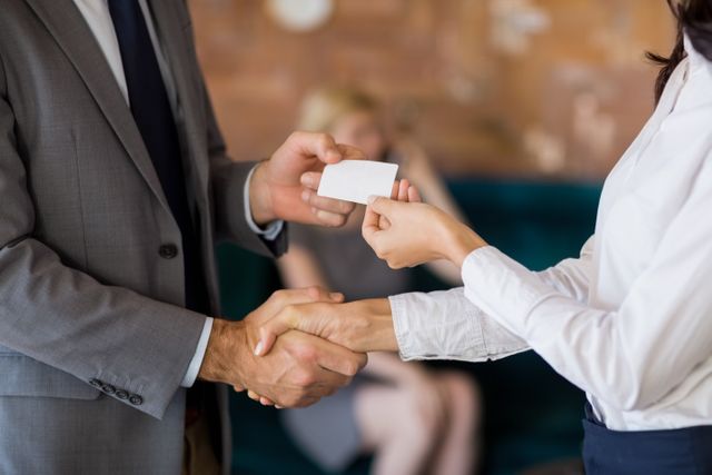 Business colleagues exchanging business card while shaking hands in a restaurant. Ideal for illustrating networking events, professional meetings, corporate partnerships, and business introductions. Can be used in articles, blogs, and presentations about business etiquette, networking tips, and professional relationships.