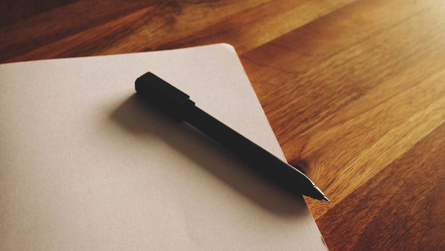 Black pen laying on sheet of blank paper on wooden table. Suitable for office, writing, or stationery-related content. Great for blog posts on planning, writing inspiration, or stationery reviews.