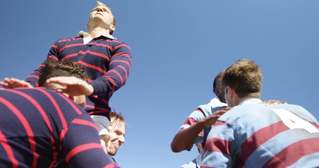A group of young Caucasian men engage in a rugby line-out under a clear blue sky, with copy space. Their athletic endeavor captures the essence of teamwork and competitive sports.