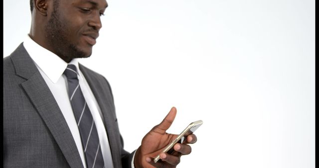 A young African American businessman in a suit is focused on his smartphone, with copy space. His engagement with the device suggests he might be checking important work emails or scheduling meetings.
