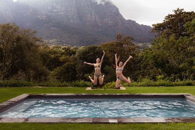 Two friends are jumping into a swimming pool in a backyard with a stunning mountain view. This image captures the essence of summer fun and outdoor activities. Ideal for use in travel brochures, vacation advertisements, lifestyle blogs, and social media posts promoting leisure and relaxation.