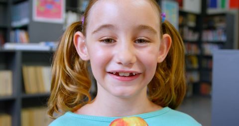 Smiling Young Girl Holding Apple in School Library