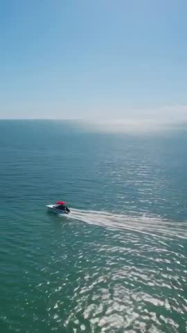 Vertical drone footage of speedboat with red canopy skimming calm turquoise sea leaving white wake