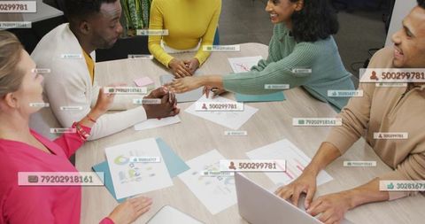 Diverse team collaborating around table with data charts, laptop and digital labels